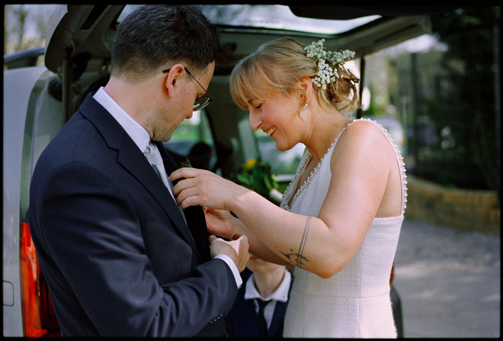 The bride pinning the groom's boutonnière by the car