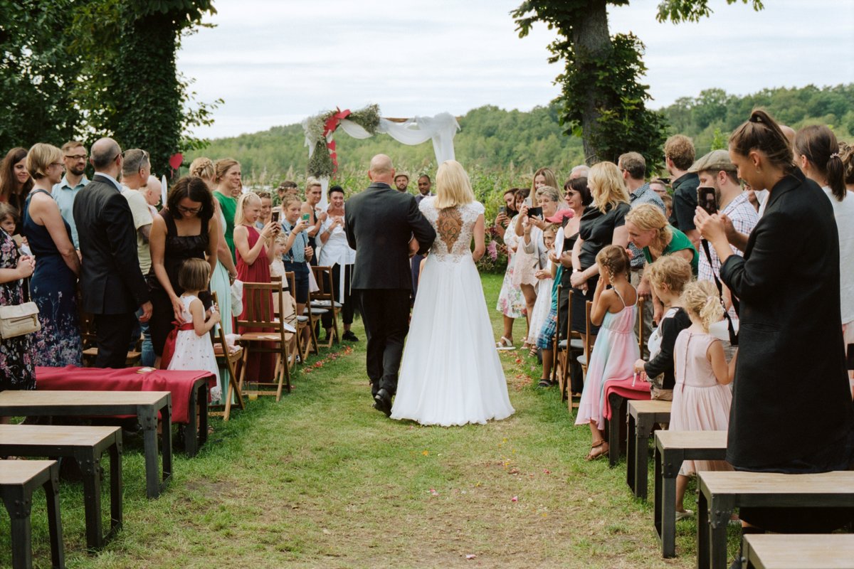 The wide garden aisle lined with guests before the lake
