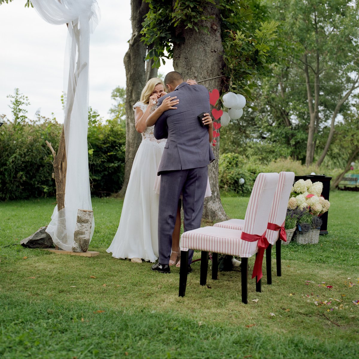 The couple embracing beneath a tree hung with ribbons