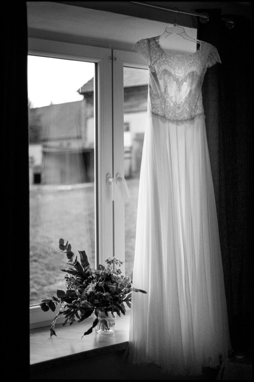 Das Hochzeitskleid hängt im Fenster, mit Brautstrauß, in Schwarz-Weiß