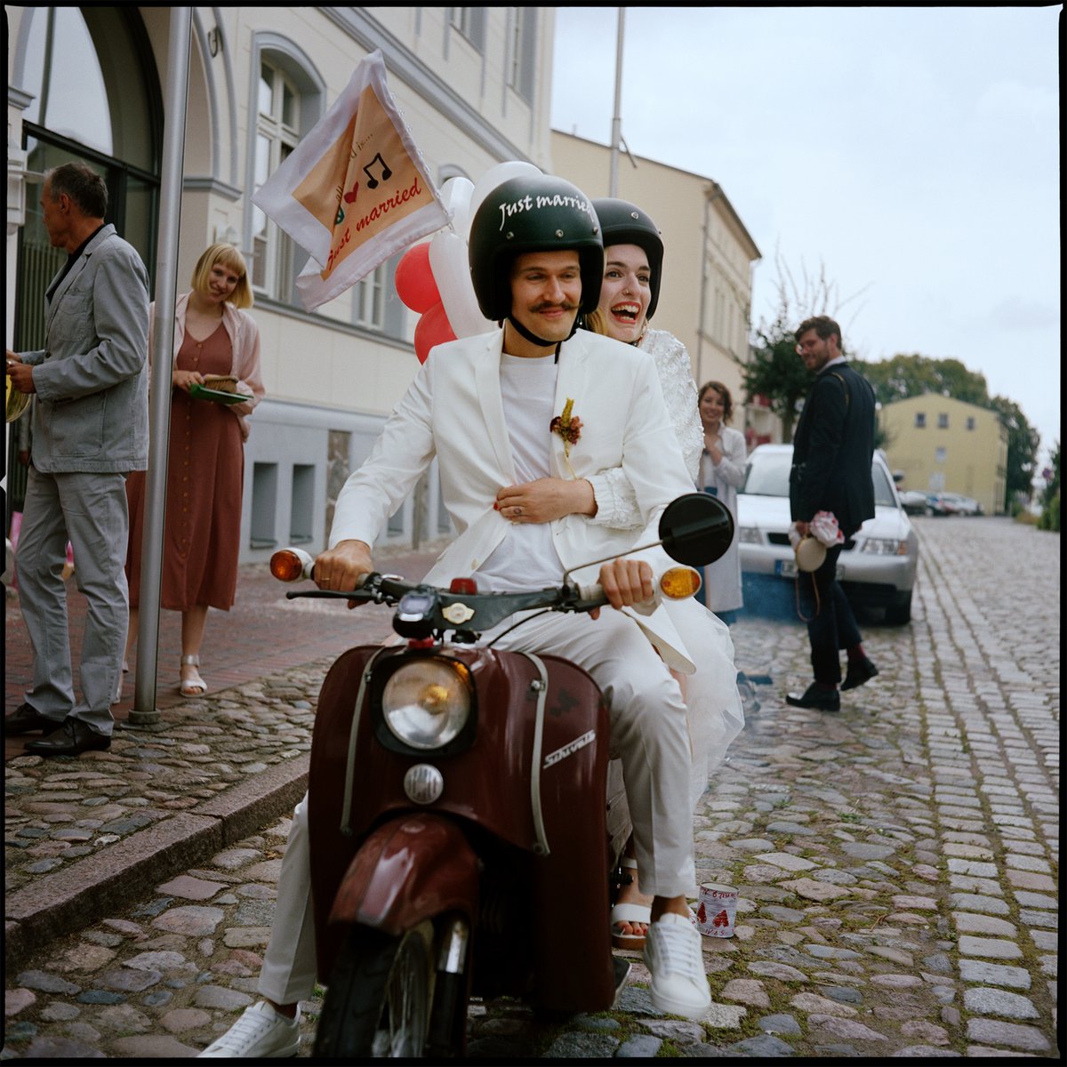Das Paar fährt auf einem Vintage-Roller über das Kopfsteinpflaster