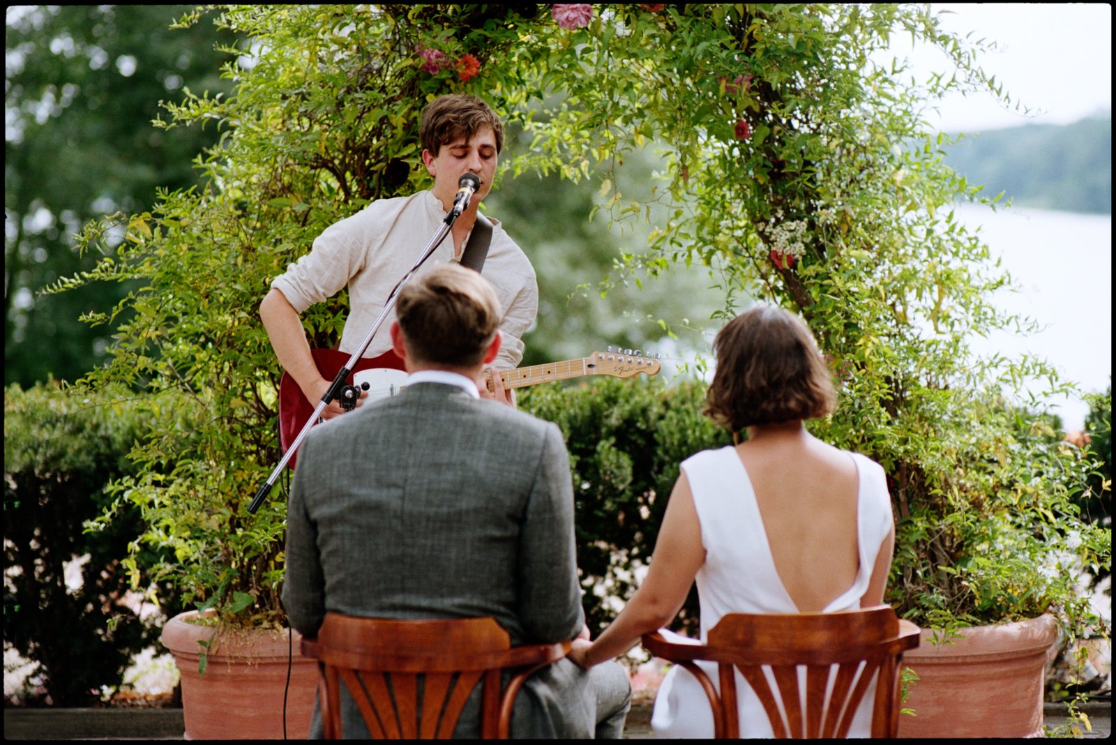 Ein Musiker spielt, während das Paar zuschaut, am Wasser, Hochzeit von Suelyn & Pascal in Groß Glienicke, Potsdam