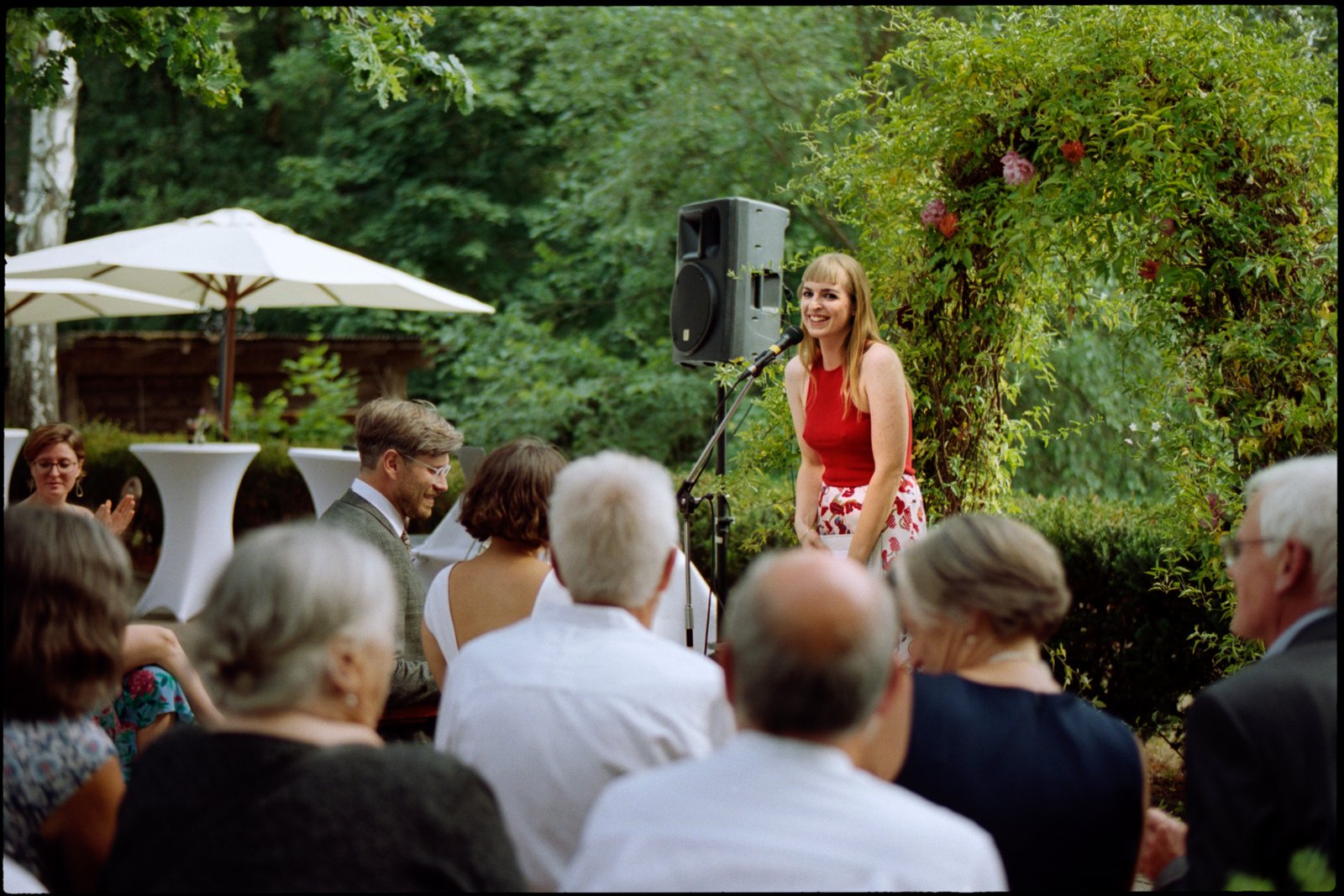 Ein Gast hält eine Lesung vor den sitzenden Gästen im Garten, Hochzeit von Suelyn & Pascal in Groß Glienicke, Potsdam