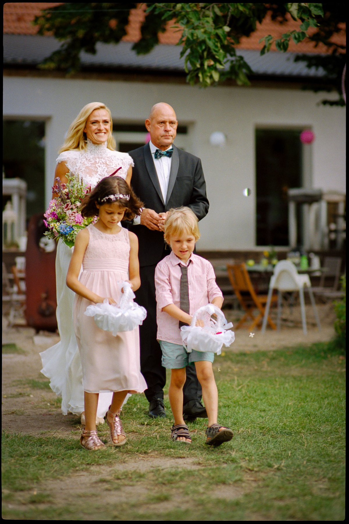Flower girl and page boy leading the couple through a summer garden, 35mm film photograph by Martina Manz