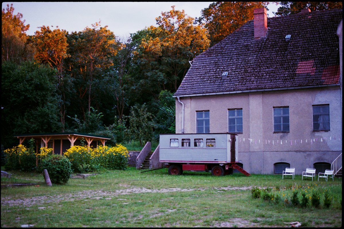Hochzeitslocation auf dem Land im Abendlicht, Wimpelkette an der Wand und ein alter Bauwagen auf der Wiese