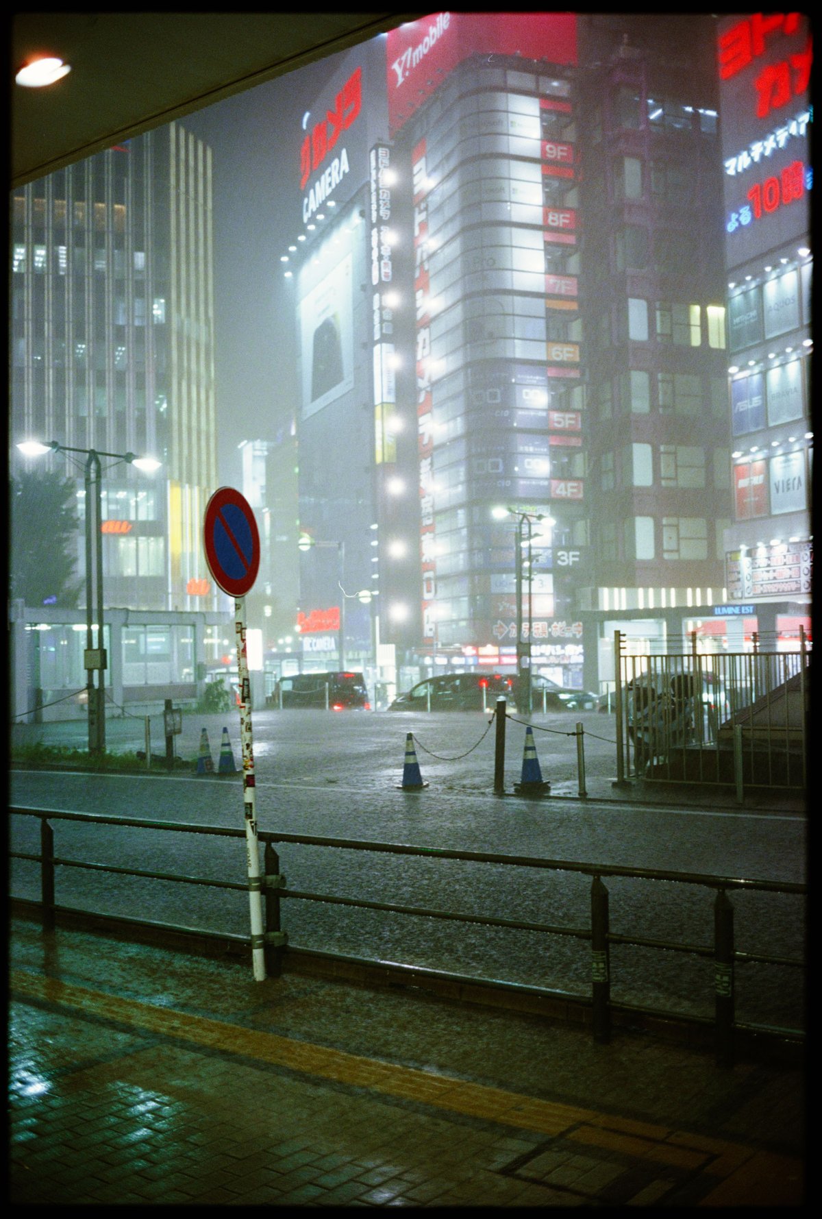 Nächtlicher Platzregen am Ostausgang des Bahnhofs Shinjuku, Leuchtreklamen im Regendunst