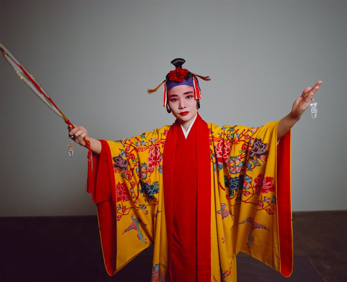 Eine Tänzerin mit ausgebreiteten Armen in einem gelb-roten Kimono