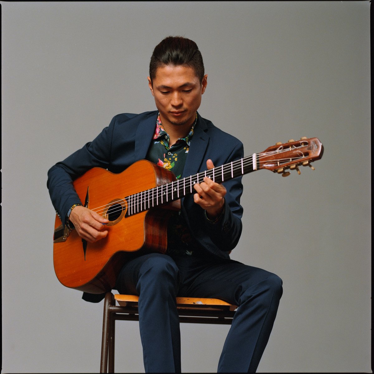 Ein Musiker sitzt im blauen Anzug und spielt akustische Gitarre, analoges Filmportrait
