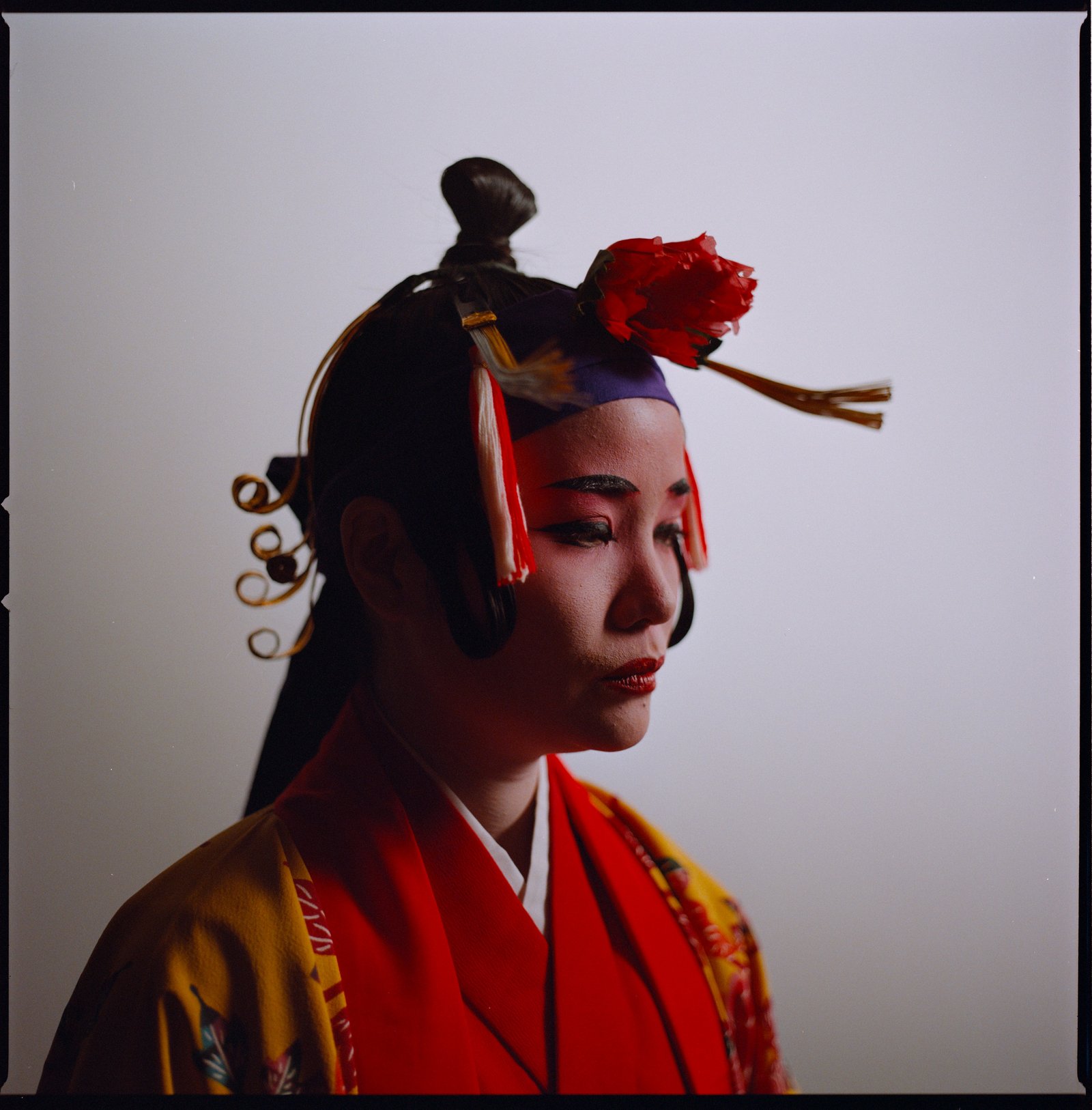 Eine Darstellerin im Profil in rot-goldenem Ryukyu-Kostüm mit Blumenkopfschmuck, analoges Filmportrait von Martina Manz, Berlin