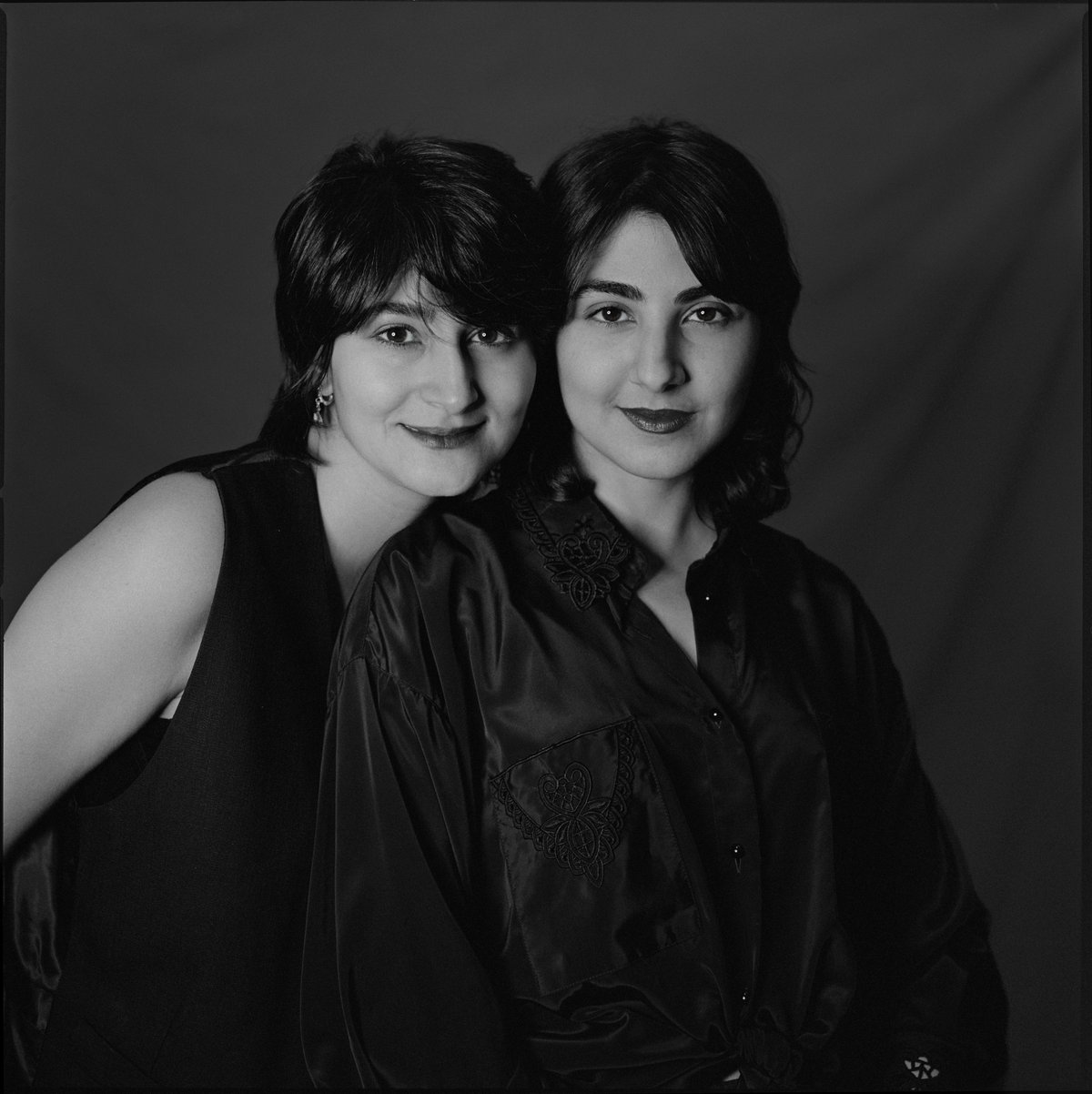 Zwei Frauen in dunkler Kleidung stehen eng beieinander vor dunklem Hintergrund, schwarz-weiß, analoges Filmportrait